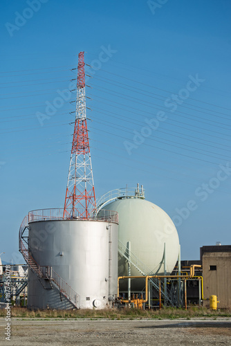 送電鉄塔と下水処理場の工業用タンク・青空に映える都市インフラとエネルギー設備景観