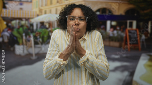 Valokuva Woman wearing yellow striped shirt hugging herself with tense expression on restaurant terrace outdoors; discomfort