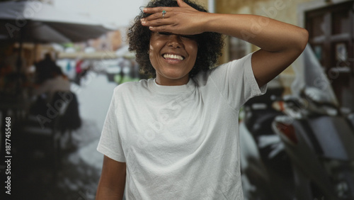 Foto Young african american woman in white tshirt covers eyes with hand on bustling city street; embarrassment