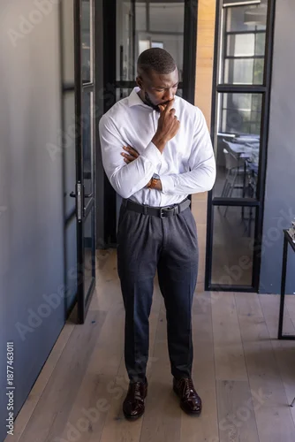 Fototapeta Corporate professional standing in office corridor, with black metal glass doors, wood floor