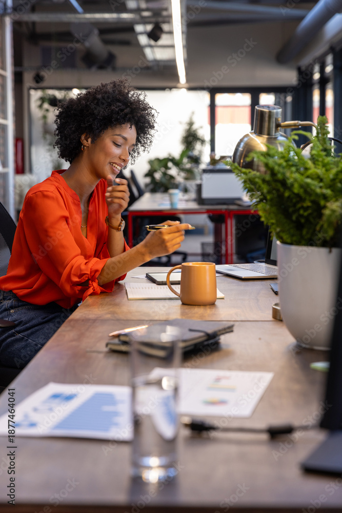 Fototapeta premium African american woman writing in notebook and checking laptop at office, copy space