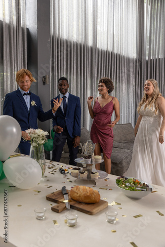 Diverse wedding party posing in modern lounge venue with bouquet by table with cupcakes