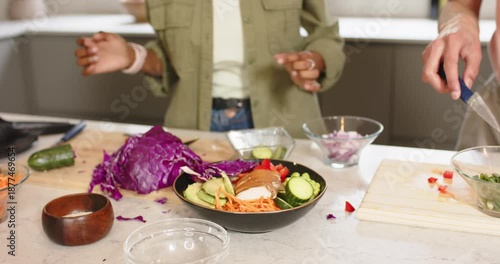 Diverse friends finishing salad in black bowl, chopping peppers and testing seasoning on counter