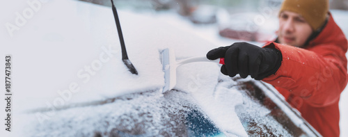 фотографія man in winter clothes clean ice and snow from car's windshield with scraper warming up car parked on residential street cold morning