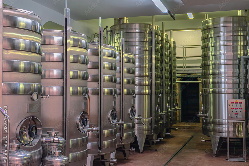 Fototapeta premium Steel Fermentation Tanks at winery. Stainless steel fermentation tanks at winery used for wine production and storage during harvest season. Industrial wine technology and clean production process