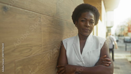 Foto Woman leaning against wooden wall with arms crossed on street, slight smile and relaxed posture; resilience confidence