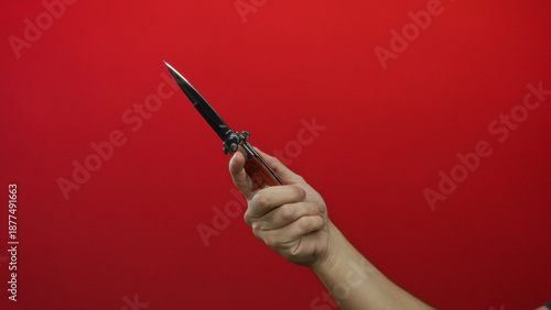 Billede på lærred Man holding knife against red background with isolated hand capturing sharp blade and dramatic contrast