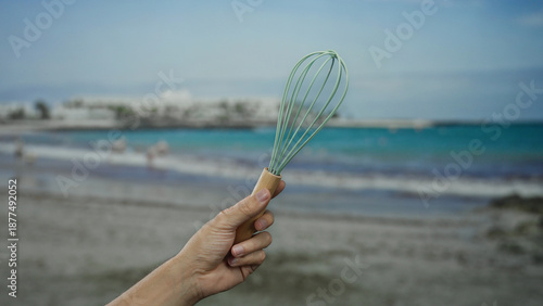 Hand of a man holding a whisk on a beach with the sea in the background, capturing a unique seaside scene.