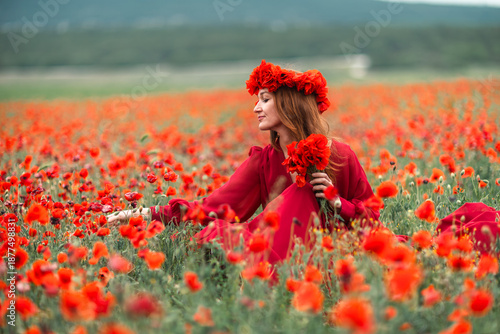 Billede på lærred Woman poppies field sitting in long red dress wearing floral crown on a summer d