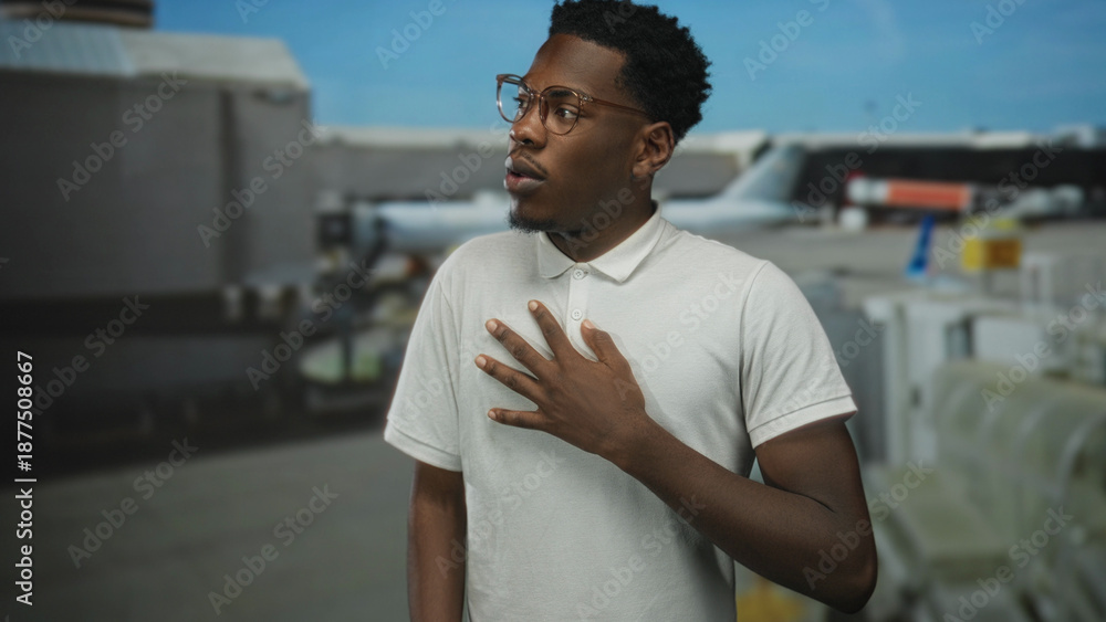 Fototapeta premium Man hand on chest stands at airport terminal outdoors by parked plane under bright blue sky; surprise astonishment wonder shock.