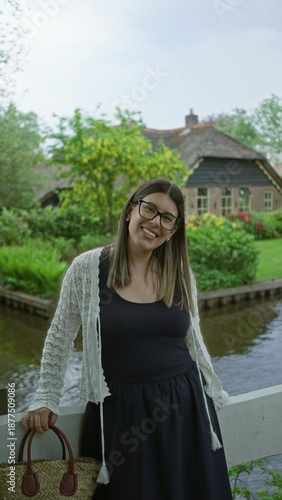 Canvastavla Woman smiling by a canal in giethoorn netherlands, wearing a dress with a scenic view of greenery and traditional houses in the background on a tranquil day