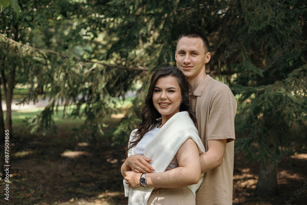Fototapeta premium Portrait of a young couple in love hugging and kissing in a park. Romantic relationship between a man and a woman. Copy space