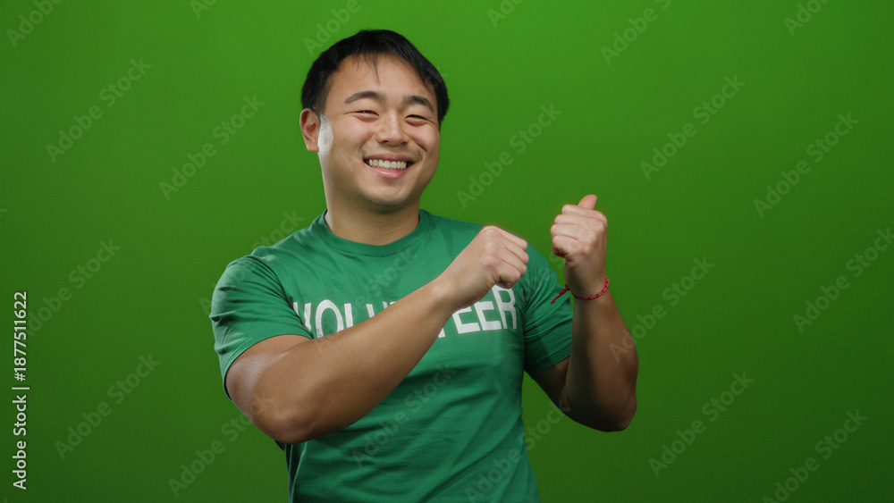 Fototapeta premium Young man in volunteer shirt smiles over green background, expressing positivity and energy.