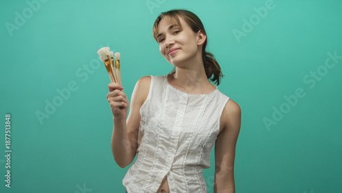 Fotografía Woman holding a fan of paintbrushes and kissing the bristles in a turquoise studio while smiling and posing; creative playfulness