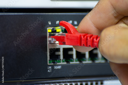 Close-up of a hand plugging a red ethernet cable into a network switch or router. Concept of data connection, internet technology, and IT infrastructure.