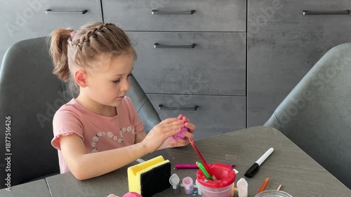 Little girl decorating Easter eggs with colorful stickers while sitting at table at home. Creative Easter activity, simple egg decoration technique and joyful holiday preparation indoors.