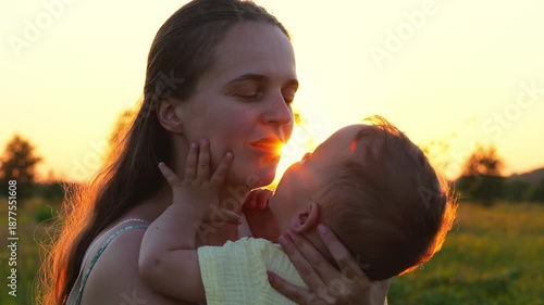 A woman smiles as she cradles her baby in her arms during sunset in a field. They share a moment of joy and connection in the warm light