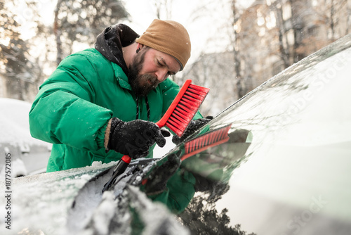 Man Brushing Snow from Area Under Car Windshield Wipers
