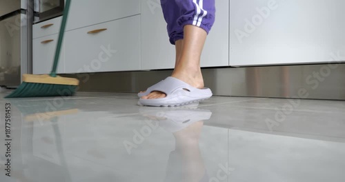Woman sweeping kitchen floor with broom in modern home interior