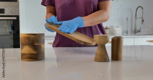 Woman cleaning stone kitchen countertop wearing protective gloves 