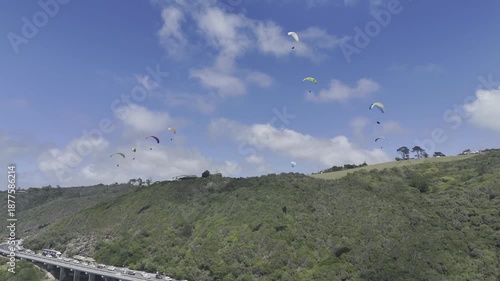 Drone orbits to the left below a sky full of paragliders on a sunny day on the Garden Route in Wilderness, South Africa