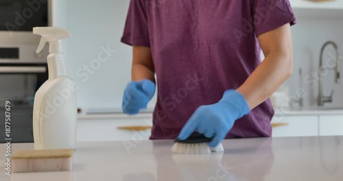 Woman cleaning stone kitchen countertop wearing protective gloves 