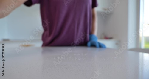 Woman cleaning stone kitchen countertop wearing protective gloves 