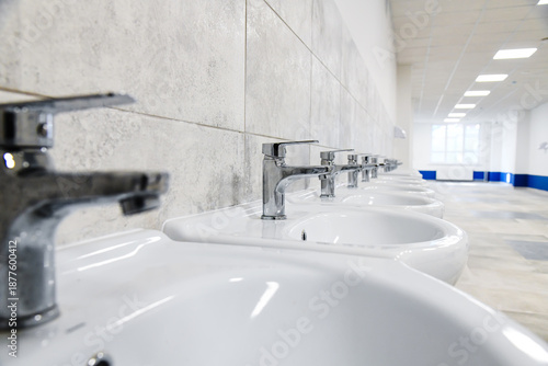 Several new and clean sinks with the same shiny chrome faucets are lined up in a row.