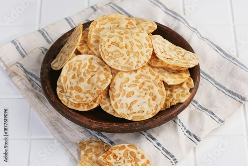 Photos Crispy Indonesian tempeh chips served on wooden plate, popular traditional snack made from fermented soybeans, crunchy texture and savory taste
