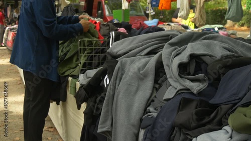 Male Shopper Looking through Pile of Used Clothes at Street Market Promoting Conscious Consumption and Eco Lifestyle
