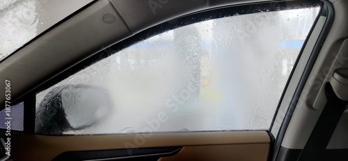 Fogged side window with water streams inside automatic car wash, interior view