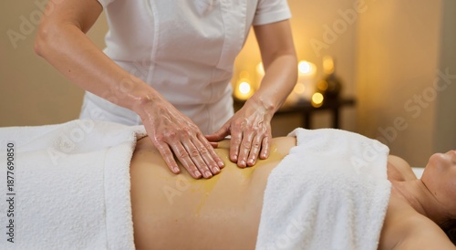 Caucasian woman enjoying a relaxing abdominal massage with oil by a masseuse. Spa treatment concept for body care and wellness.