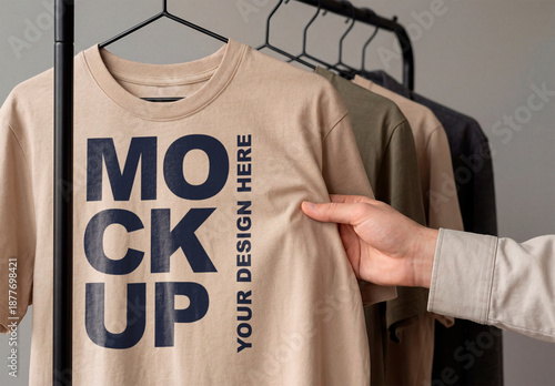 Neutral Beige T-Shirt Mockup on Clothing Rack with Hand Touching Fabric