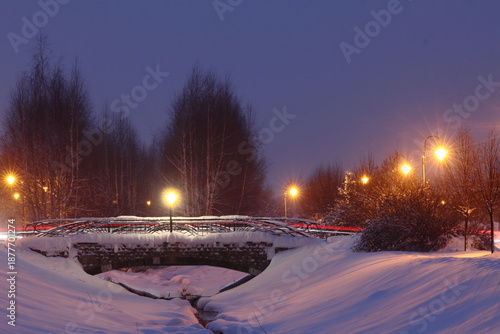 Streetlights and a bridge over a stream. Snow on the bridge and the banks of a small stream