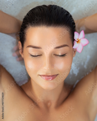 Peaceful Asian Woman Floating in Spa Water With Tropical Flower in Hair