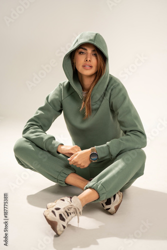 Confident young woman wearing a mint athleisure set with sweatshirt and sweatpants, posing in a minimal studio on a light background. Modern casual fashion, comfort wear, sporty lifestyle