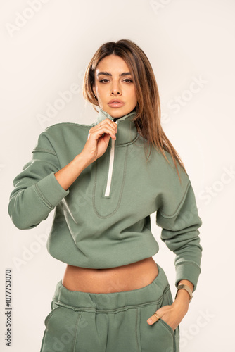Confident young woman wearing a mint athleisure set with cropped sweatshirt and sweatpants, posing in a minimal studio on a light background. 