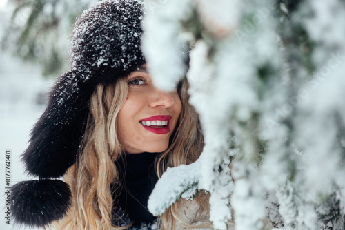 Woman stands near snowy tree in winter landscape with smile in cold weather