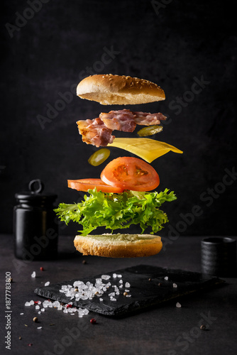 Burger on a dark background in levitation. Ingredients for a layered burger