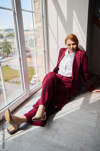 Fotografie Woman dressed in burgundy suit gazing confidently outside