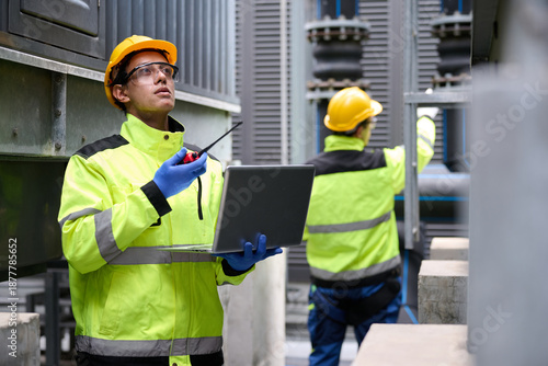 Engineers inspecting a power plant for maintenance and troubleshooting issues. They are using a laptop and radio to communicate in the factory