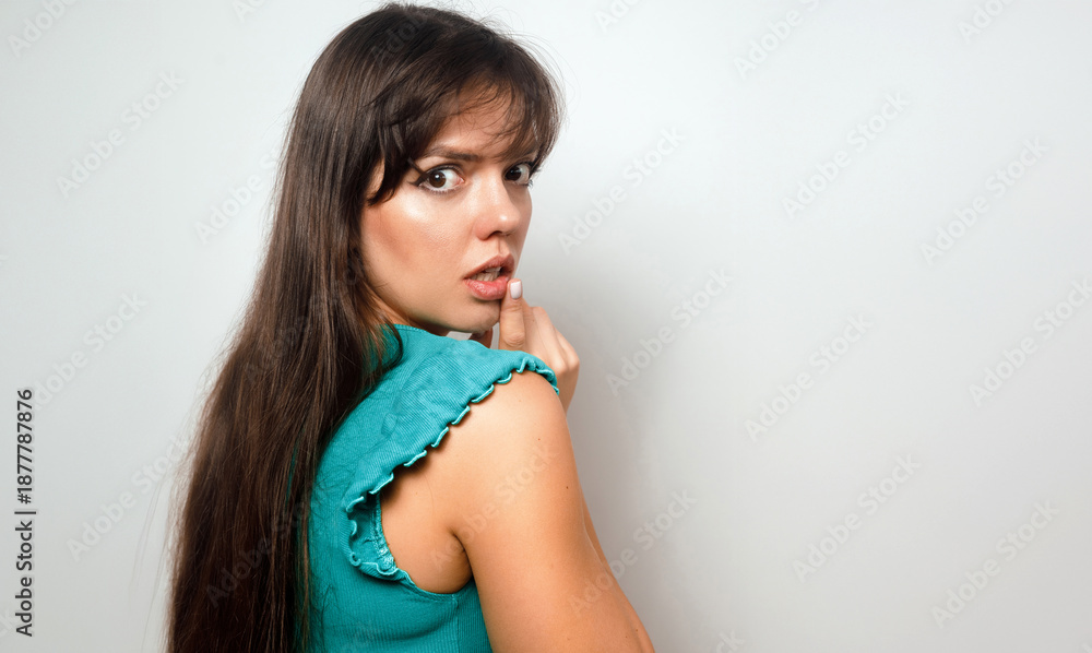 Fototapeta premium Woman looks back with surprise in a simple setting, expressing a sense of intrigue, while casually dressed with long hair and a neutral background