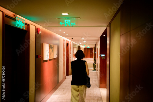 Woman walking through a hotel corridor with dim lighting and emergency exit signs. Shanghai, China