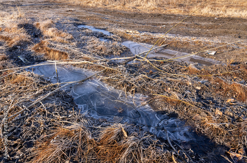 a dirt road in late autumn, covered with ice on a frosty morning

