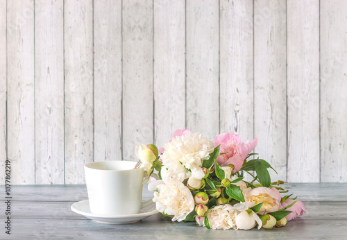 White cup of coffee or tea and bouquet of white peony flowers on a wooden table agaisnt white wooden background