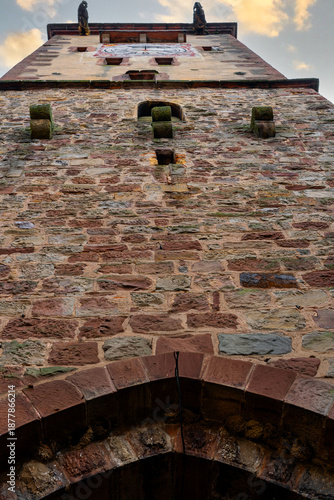 Vertical photo taken at a steep angle directly from below towards the top of an ancient medieval tower with a clock in Ribeauvillè, a village in Alsace, France.