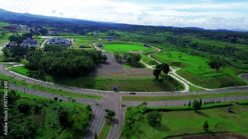 Road intersection and curved streets surrounded by green fields and open landscape, seen from aerial view.