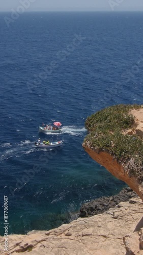 Tour boats cross paths along rocky Mediterranean shoreline. Vertical video