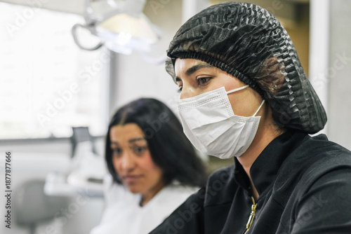 Dentist working on a computer while a female patient waits during a dental consultation in a professional clinical environment.