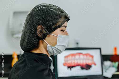 Side view of a female dentist wearing a mask with dental images displayed on a computer screen in a modern clinic.